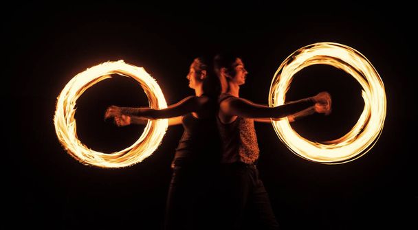 Creating awesome tracer effects. Couple of artists perform fire orbitals. Bright light trails and designs. Fire performance. Burning poi twirling. Night festival. Holiday celebration - Fotografie, Obrázek