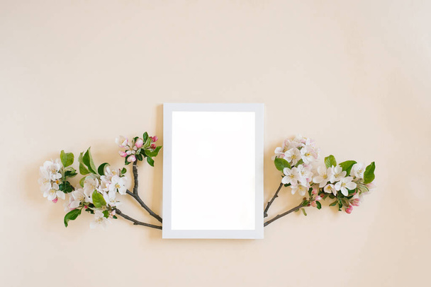 Marco blanco con espacio de copia sobre un fondo beige rodeado de ramas con flores blancas de manzana - Foto, imagen