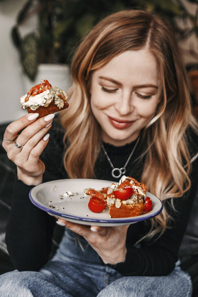Young blonde woman is eating avocado toast for breakfast in a ca - Photo, image
