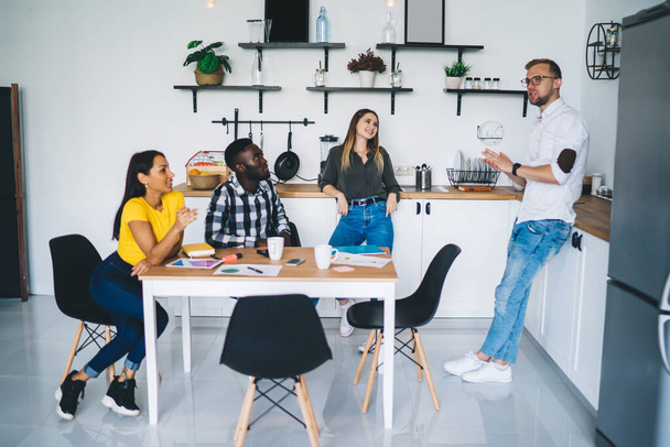 Full body of cheerful diverse colleagues in casual clothes gathering in modern kitchen and talking about business ideas during work - Foto, immagini