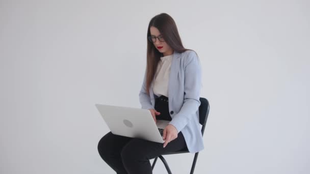 Ισχυρή αυτοπεποίθηση επιχειρηματικό ledy σε μαύρα γυαλιά κάθεται με φορητό υπολογιστή στην αγκαλιά της σε λευκό απομονωμένο φόντο και χρησιμοποιώντας touchpad - Πλάνα, βίντεο