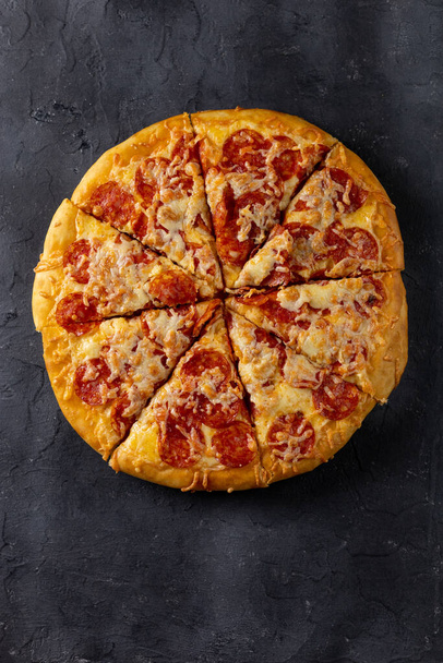 Ízletes házi pepperónis pizza sötét háttérrel. Hagyományos klasszikus pizza szalámival és sajttal. Felülnézet másolási hellyel a szöveghez. Lapos fektetés - Fotó, kép