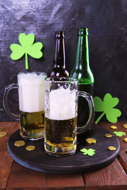 Patrick day, foamy beer in glass mugs and a bottle, gold coins on a wooden table, green shamrock on a dark background, party, congratulation, postcard - Fotoğraf, Görsel