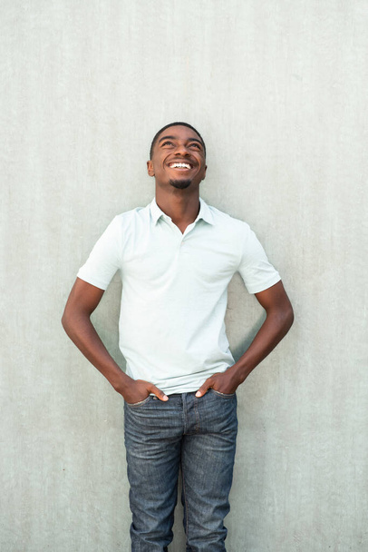 Portrait smiling young African American man standing by wall and looking up - Fotografie, Obrázek