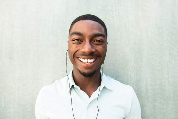 Close up front portrait smiling young African American man listening to music with earbuds  - Fotó, kép