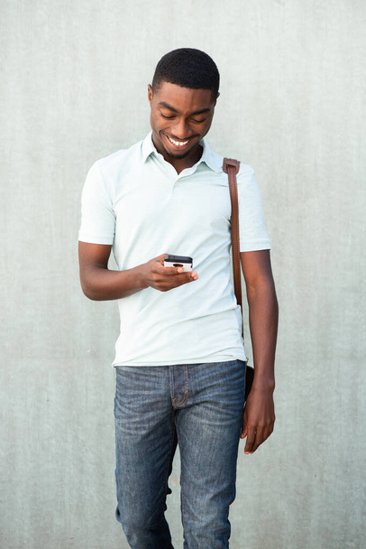 Portrait cool young black man walking with cellphone and bag - Фото, изображение