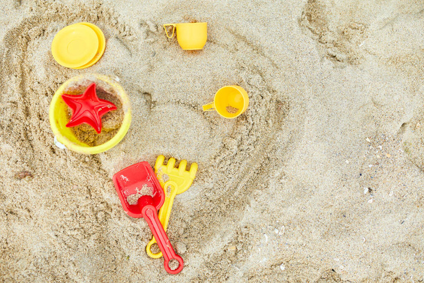 Draufsicht, flache Lage verstreuter Plastik-Strandspielzeuge auf Sandhintergrund, Familiensommerurlaub, Hintergrund mit leerem Platz für Text - Foto, Bild