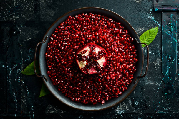 Ripe pomegranate seeds on a plate. Fresh pomegranate fruit. On a black stone background Top view. - Foto, Imagem