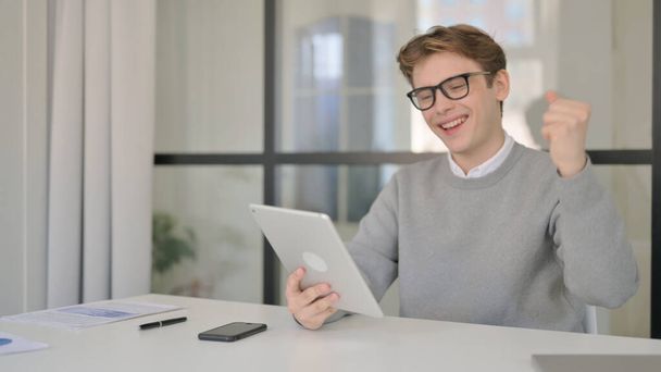 Young Man Celebrating Success on Tablet in Modern Office  - Photo, Image