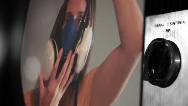 Frau setzt Atemschutzmaske auf einem Vintage-Fernseher auf. COVID-19 Globales Pandemiekonzept.  - Filmmaterial, Video