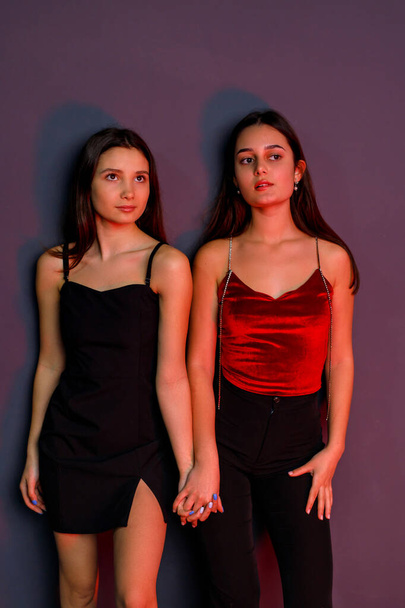 Full length photo of two elegant young women holding hands wearing black short dress and black trousers. - Photo, image