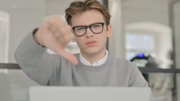 親指を下に示すノートパソコンを持つ若い男の閉鎖サイン  - 写真・画像