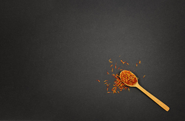 Red saffron spice in wooden spoon on black background with copy paste - Photo, image
