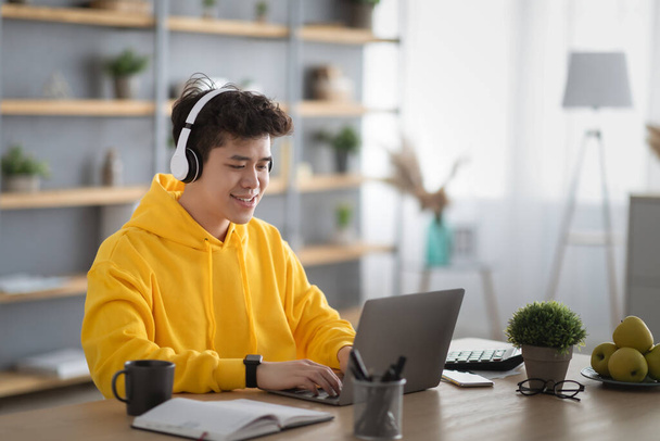 Sonriente asiático hombre en auriculares usando portátil en casa - Foto, Imagen