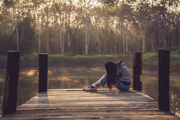 Femme en pleurs étreignant ses genoux sur un vieux pont en bois sautant dans un étang dans la nature. Femme triste et solitaire. - Photo, image