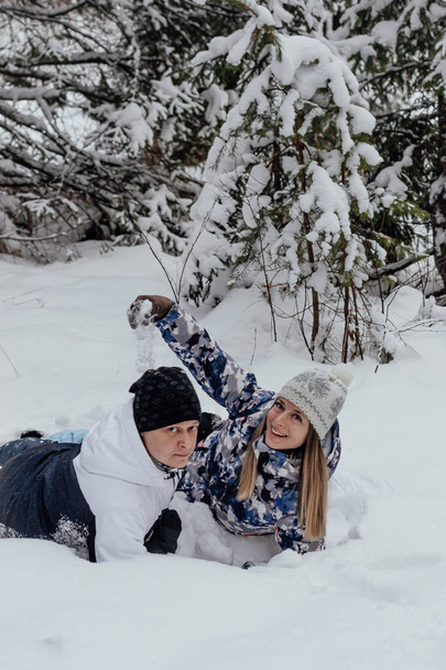 Man and woman having fun together during winter vacation. Young happy couple lies in the snow, throws snow and plays in the winter park. - Foto, Imagen
