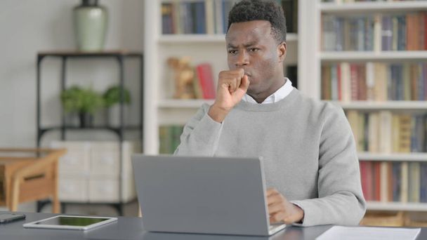 アフリカ人男性は図書館でノートパソコンを使いながら咳をする  - 写真・画像