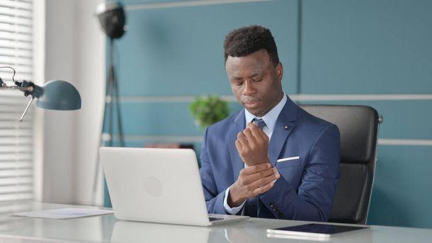オフィスでラップトップを使用している間に手首の痛みを持っているアフリカのビジネスマン  - 写真・画像