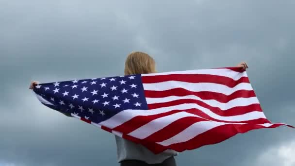 onnellinen nuori nainen, jolla on Amerikan lippu ulkona nauttien kauniista luontonäkymistä vuoren huipulla auringonlaskun taustalla. Menestys, vaeltaminen ja urheilu käsite. - Materiaali, video