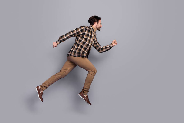 Photo of funky pretty man wear plaid shirt jumping high running fast empty space isolated grey color background - Фото, изображение