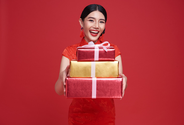 Happy Asian woman wearing traditional cheongsam qipao dress holding gift box isolated on red background. Happy Chinese new year - Photo, Image