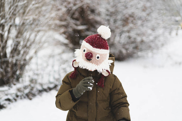 Милий маленький хлопчик у смішному зимовому капелюсі ходить під час снігопаду. На відкритому повітрі зимові заходи для дітей
. - Фото, зображення