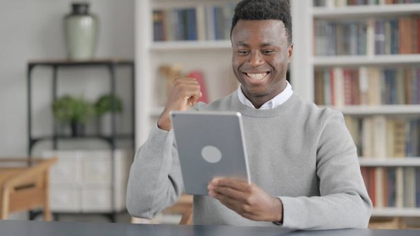 Африканський чоловік святкує успіх на планшеті в бібліотеці
  - Фото, зображення