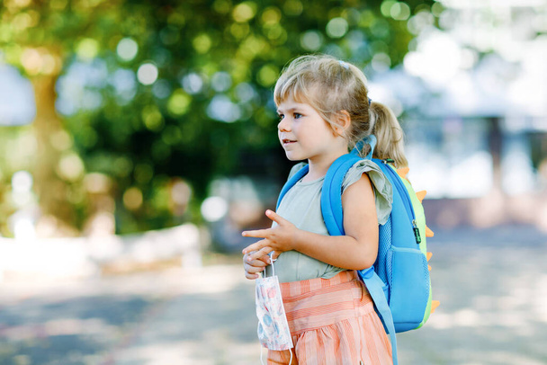 Malá batolátko dívka na její první den na cestě do školy s lékařskou maskou proti viru koróna covid. Zdravé krásné dítě chodí do školky a školky. Šťastné dítě s batohem - Fotografie, Obrázek