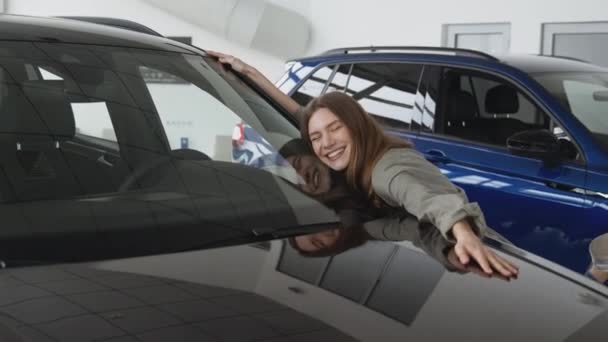 Happy owner. Young excited woman hugging new car, enjoying long awaited vehicle purchase at dealership salon, zoom in - Materiał filmowy, wideo