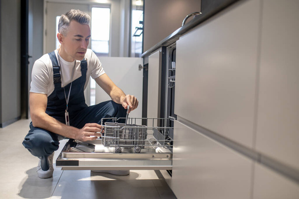 Man crouching down opening dishwasher inspecting - Foto, immagini