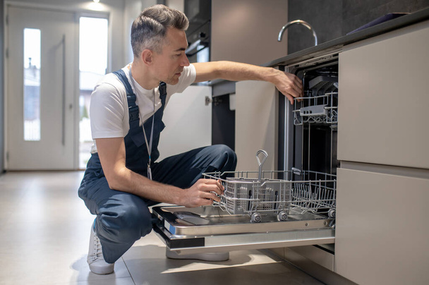 Man carefully examining an open dishwasher - Фото, зображення