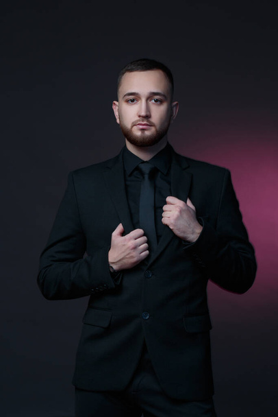 Young handsome man with a beard in a black classic suit on a dark background. - Foto, Imagen