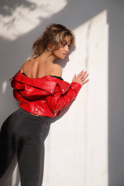 Sensual slender girl in a red jacket on a naked body, view from the back near the wall in the rays of the bright sun. - Foto, Imagem