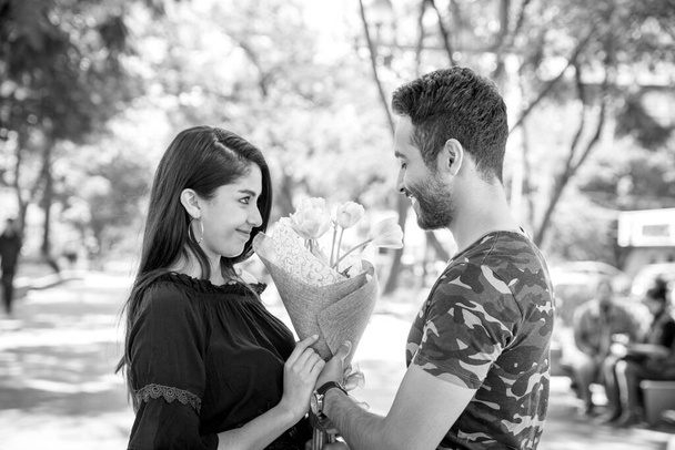 Young man handing flowers to his girlfriend in the park. - Φωτογραφία, εικόνα