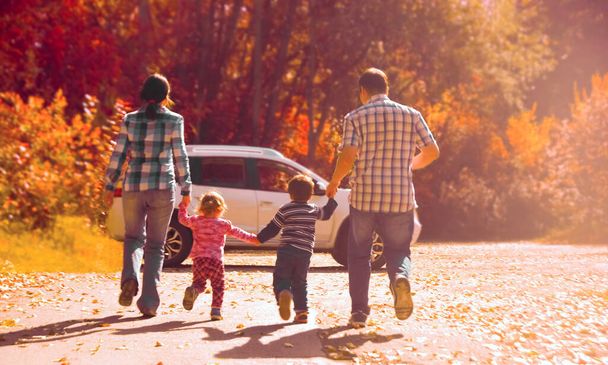 Happy family. Parents - mother, father and kids - daughter, son holding hands each other on white SUV big car. Casual dress. Sunset light rays. Outdoor photo in autumn park.  - Photo, Image