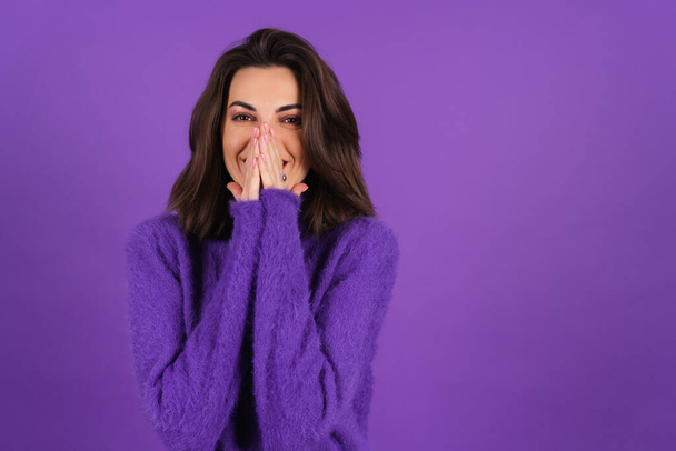 Young woman in a purple soft cozy sweater on the background is cute, in high spirits, laughs shyly, covering her mouth with her hands - Foto, Bild