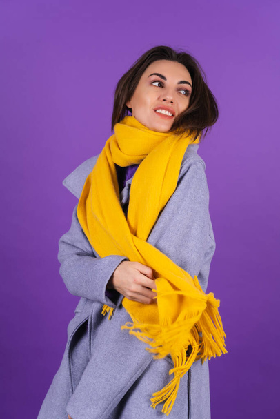 Young woman in a gray coat and a yellow scarf on a purple background posing cheerfully, cozy and warm, autumn winter style - Φωτογραφία, εικόνα