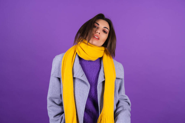Young woman in a gray coat and a yellow scarf on a purple background posing, cozy and warm, autumn winter style - Foto, Bild