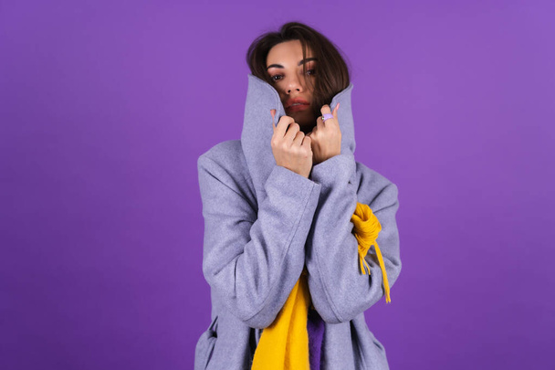 Young woman in a gray coat and a yellow scarf on a purple background posing, cozy and warm, autumn winter style - Photo, image