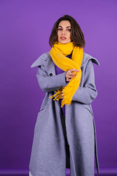 Young woman in a gray coat and a yellow scarf on a purple background posing, cozy and warm, autumn winter style - Photo, Image