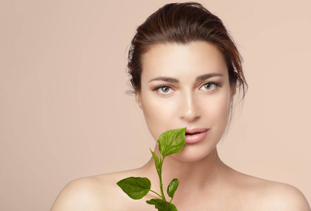 Natural Beauty and Skin Care. Beautiful young woman with clean fresh skin and green leaves near to face. - Fotó, kép