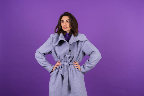 Young woman in a gray coat on a purple background posing, cozy and warm, autumn winter style - 写真・画像