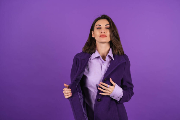 Young woman in a woolen coat on a purple background posing, cozy and warm, autumn-winter style, smiling confidently with lipstick on her lips - Fotoğraf, Görsel