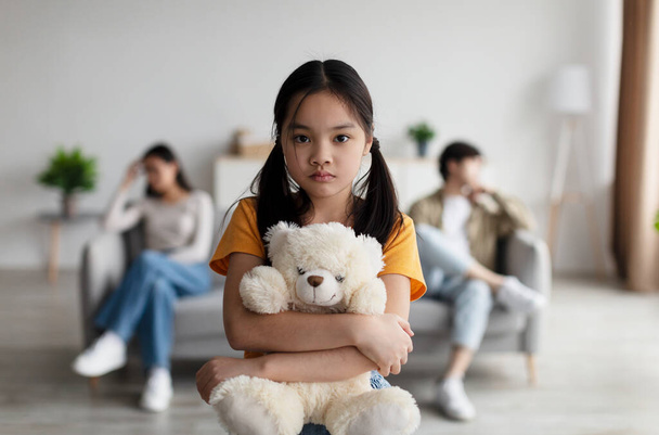 Depressed japanese adolescence girl hugs toy. Offended young wife ignores husband, sits on sofa in living room - Foto, Bild