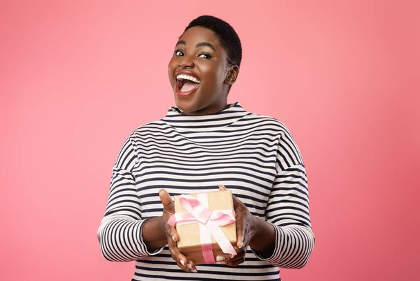Excited African Woman Giving Present To Camera Over Pink Background - Foto, imagen