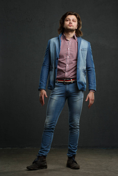An attractive white man in jeans stands in full growth against a dark background. - Foto, Imagen
