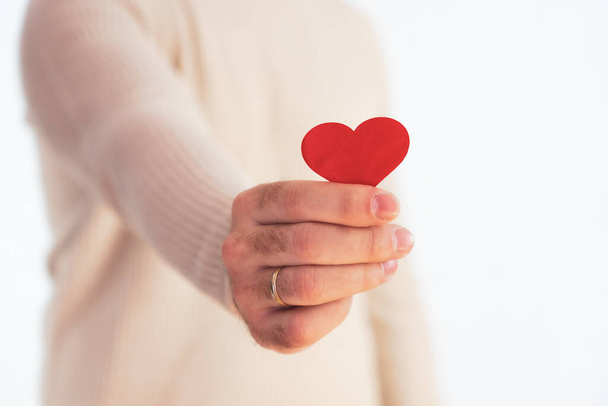 Small red heart held by an unrecognizable man's hand on a white background - Foto, imagen