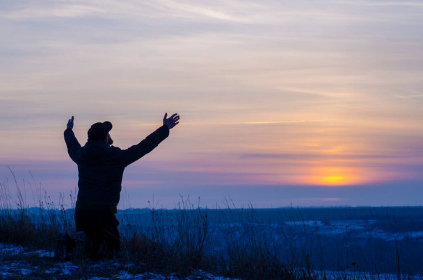 Prayer. Repentance. Silhouetted men on a background of blue sky and sunset. Kneeling Prayer to God. Glorification. Praising God - Photo, image