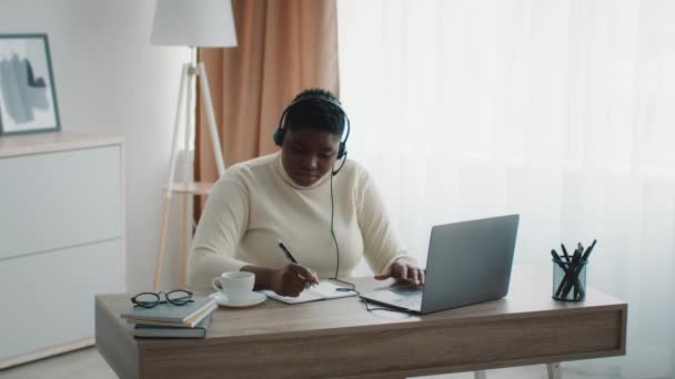 Surpoids dame africaine à l'aide d'un ordinateur portable prenant des notes dans le bureau - Séquence, vidéo