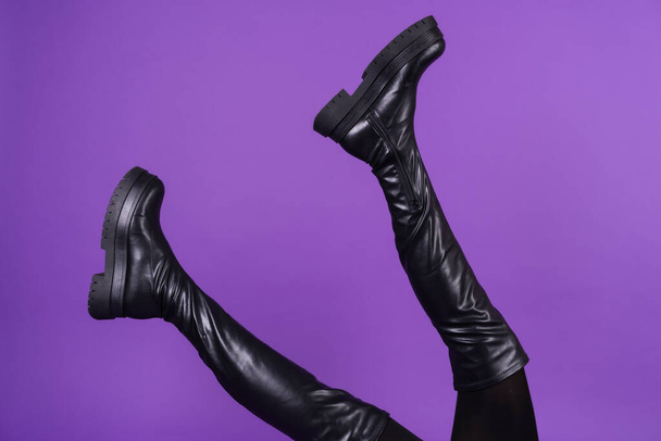 Beautiful long thin legs in high leather black boots on a purple background - Foto, immagini